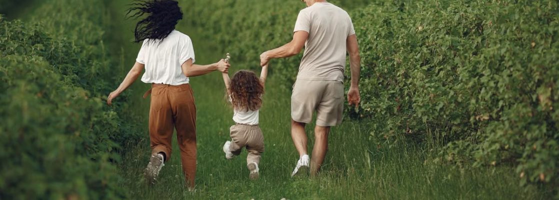 A joyful family strolls through a lush green field, enjoying quality time together.
